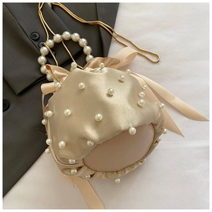 Close-up of champagne satin bucket bag with pearl handle and elegant bow drawstring