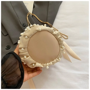 Detailed close-up of champagne satin pleated bucket bag with white pearl trim and gold chain
