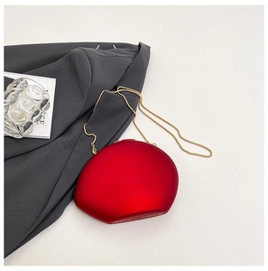 Top view of a burgundy oval hard-shell evening bag with gold snake chain and suit background