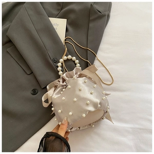 Detail of champagne satin bucket bag with pearl handle, chain strap, and bow accents