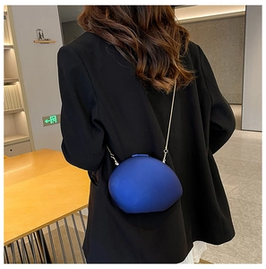 Detail of dark blue matte egg-shaped clutch bag with golden metal chain strap on model