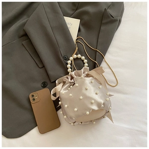 Detail of satin bucket bag with faux pearls, golden chain strap and round pearl handle