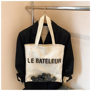 Close-up of clear PVC and canvas tote bag featuring LE BATELEUR print on a hanger