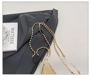 Detailed macro of a golden bead chain strap with a mini shell-shaped metal pendant