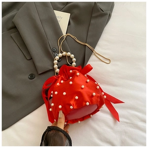 Detail of red satin drawstring bucket bag with pearls, golden chain and bow decoration