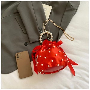 Detail of red satin bucket bag with pearl embellishments and silk bow on textured background