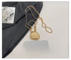 Detailed macro view of a golden shell pendant and round bead chain on fabric surface