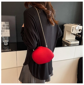Detail of red oval acrylic clutch bag with gold chain strap on a model's back