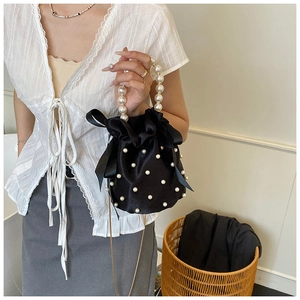 Detail of black satin bucket bag with faux pearl embellishments and a chunky pearl handle
