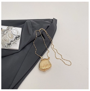 Detailed view of mini golden shell-shaped metal bag on grey fabric with pearl chain