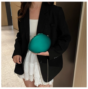 Detail of emerald green oval acrylic clutch with gold chain strap on a fashion model