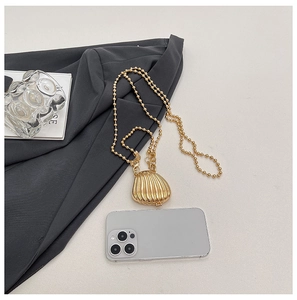 Detailed close-up of mini gold shell bag with metallic bead chain on gray fabric