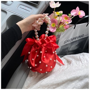 Detail of red satin bucket bag with pearl handle, drawstring closure and silk bow