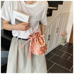Detail of pink satin bucket bag with pearl embellishments and golden metal chain strap