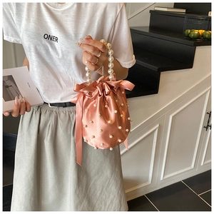 Detail of pink satin bucket bag featuring pearl handles and elegant ribbon bow detail