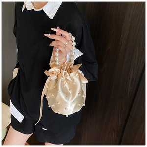 Detail of champagne satin bucket bag with pearl embellishments and a pearl handle