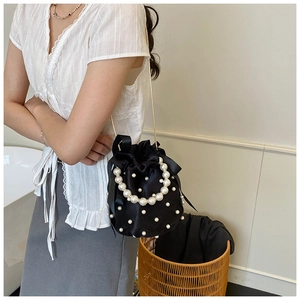 Detailed close-up of a black satin bucket bag with pearls and gold metal chain strap