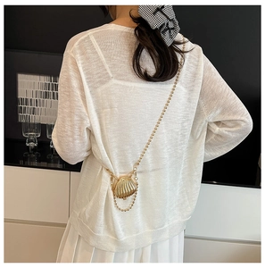 Detail shot of a mini shell crossbody bag with golden chain on a white knit outfit