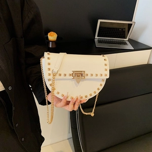 Modern white saddle bag with golden studs and chain strap in a lifestyle setting