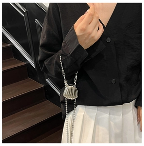 Mini silver shell-shaped metal bag with wave texture and long bead chain on a model