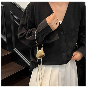 Detail of a mini shell-shaped gold metal crossbody bag with a beaded chain strap
