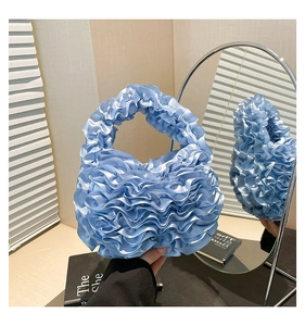 Close-up of light blue ruffle handbag with pleated satin texture and wave design