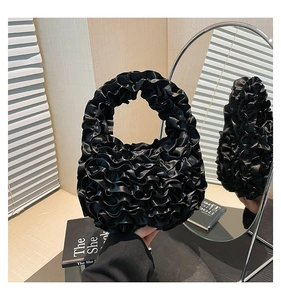 Detail of elegant black pleated ruffle handbag with a glossy satin finish and chic handle