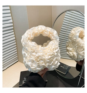 Close-up of elegant creamy white satin pleated handbag with decorative lace ruffles