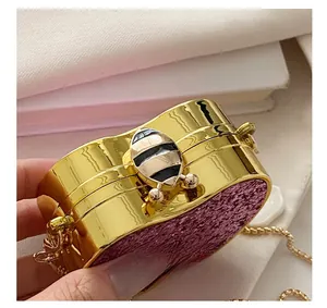Detailed close-up of golden bee clasp and purple glitter finish on evening clutch bag