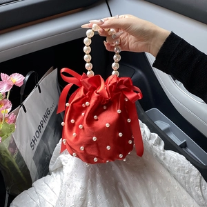 Red satin drawstring bucket bag with elegant pearl handle and silk bow accents