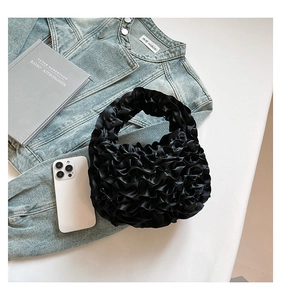 Detailed look at black pleated satin handbag with ruffles on a casual denim background