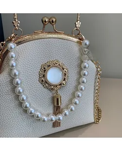 Detailed macro view of ivory faux leather bag featuring pearl handle and gold tassel