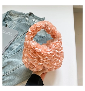 Detail of pink satin handbag with ruffle pleated design held against denim jacket