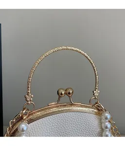 Detail of white lychee leather shell bag with pearl decor and embossed metal handle