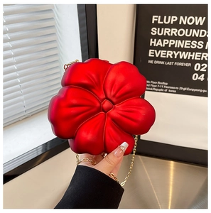 Detail of red flower crossbody bag with gold chain strap held against a neutral backdrop
