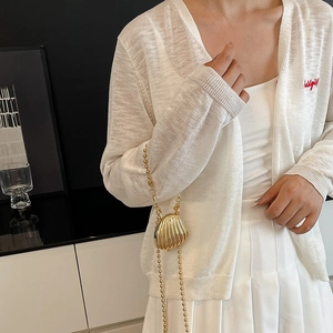 Mini gold shell chain bag for women paired with a white knit cardigan and pleated skirt