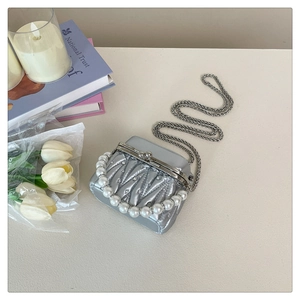Detail of silver quilted mini bag with pearl handle and metal chain on a desktop