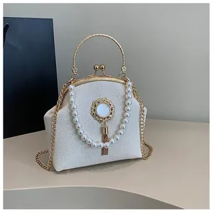 Detail of lychee textured leather shell bag with pearl decor and gold metallic clasp
