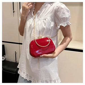 Detailed view of red glossy evening bag with gold metal handle and chain strap