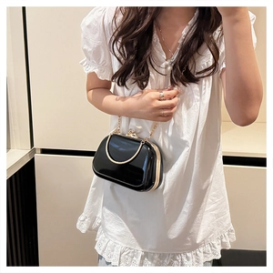 Glossy black patent leather evening bag with golden circular handle and chain on model