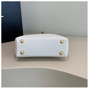 Detailed bottom view of white lychee leather handbag featuring four gold metal feet