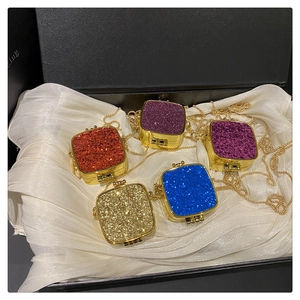Close-up of mini glitter acrylic purses in five colors with gold chain straps in a gift box