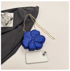 Deep blue acrylic flower crossbody bag with gold chain strap shown next to smartphone