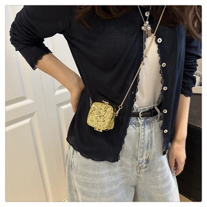 Detail of glittery gold mini crossbody bag with metal chain shown on model wearing denim
