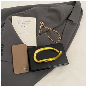 Flat lay of a black rectangular acrylic clutch featuring a thick gold organic handle and chain