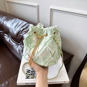 Detail of mint green denim bucket bag with frayed edges, gold chain, and pearl charm