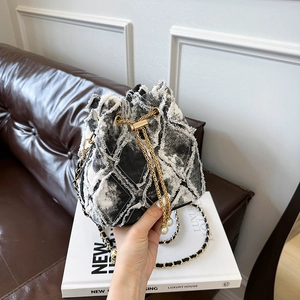 Detail of frayed edge denim bucket bag with quilted pattern, gold chain and pearl charms