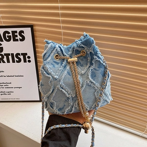 Detail of light blue denim bucket bag with quilted rhombus pattern and chain strap