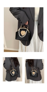 Detail of elegant black faux leather bag with pearl handle and golden heart clasp lock