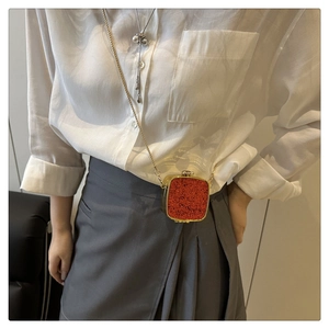 Detail of red sequin acrylic mini box bag with gold chain strap on a white shirt model